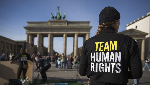 Ein Person mit einem Pulli, auf dem steht: „Team Human Rights“, im Hintergrund das Brandenburger Tor.